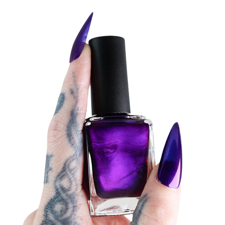 Purple nail polish bottle held by a hand with purple nails against a white background