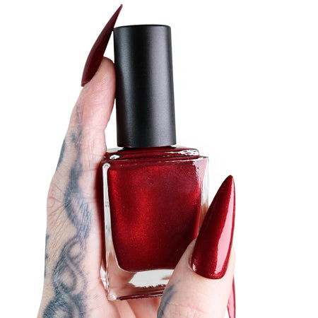 Red nail polish bottle held by a hand with red nails on a white background